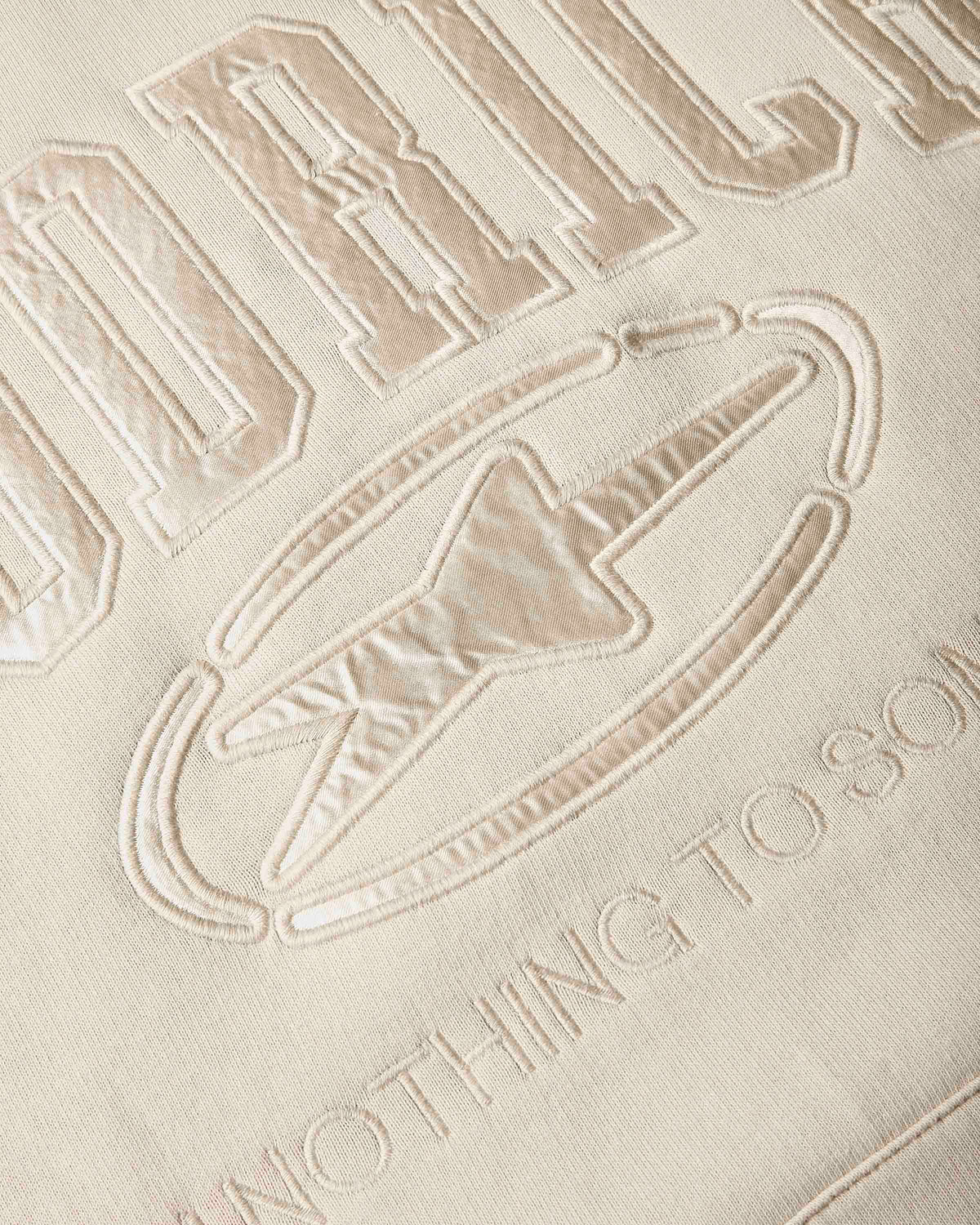 Close-up of a beige embroidered fabric with the Hoodrich branding