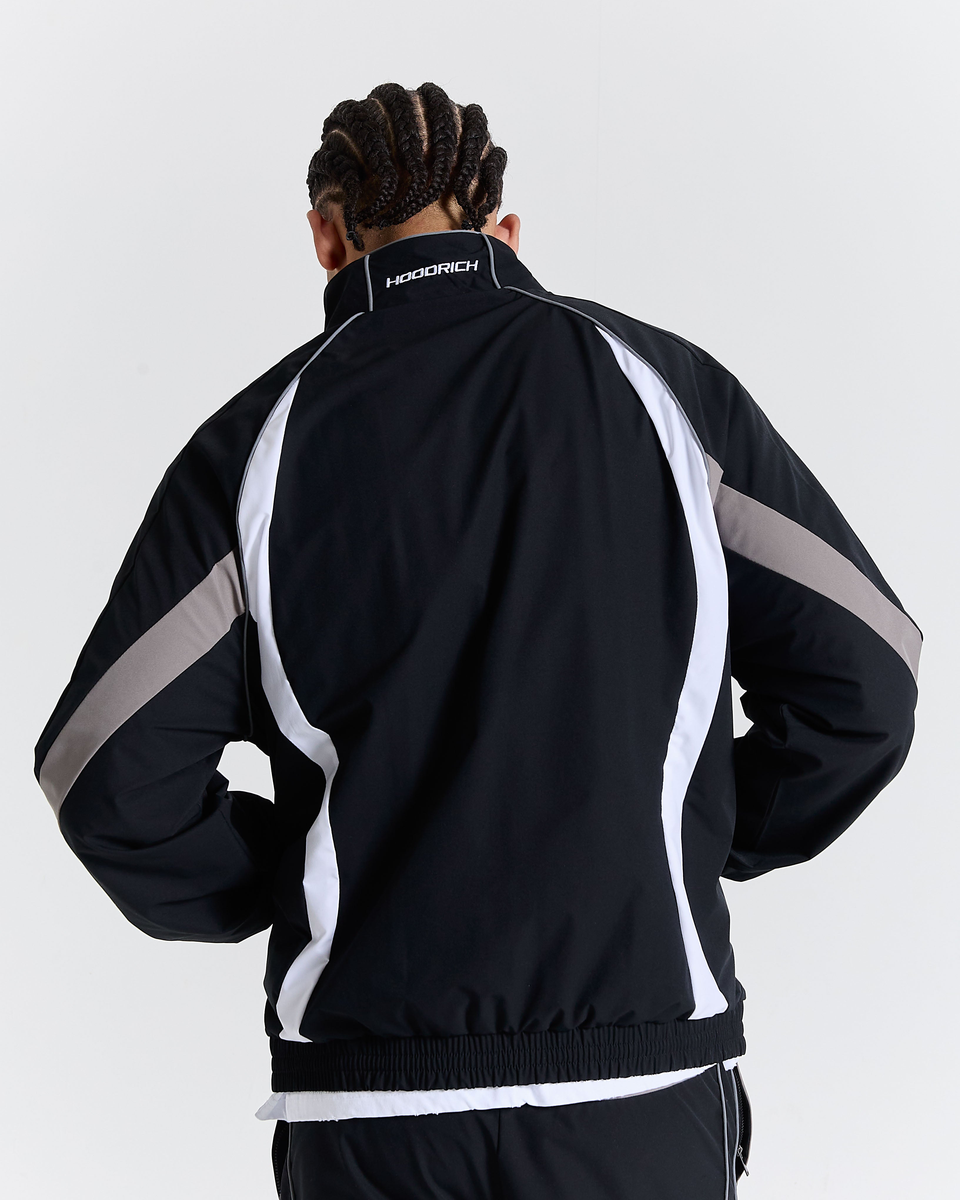 Person wearing a black tracksuit with white and gray accents on a light gray background