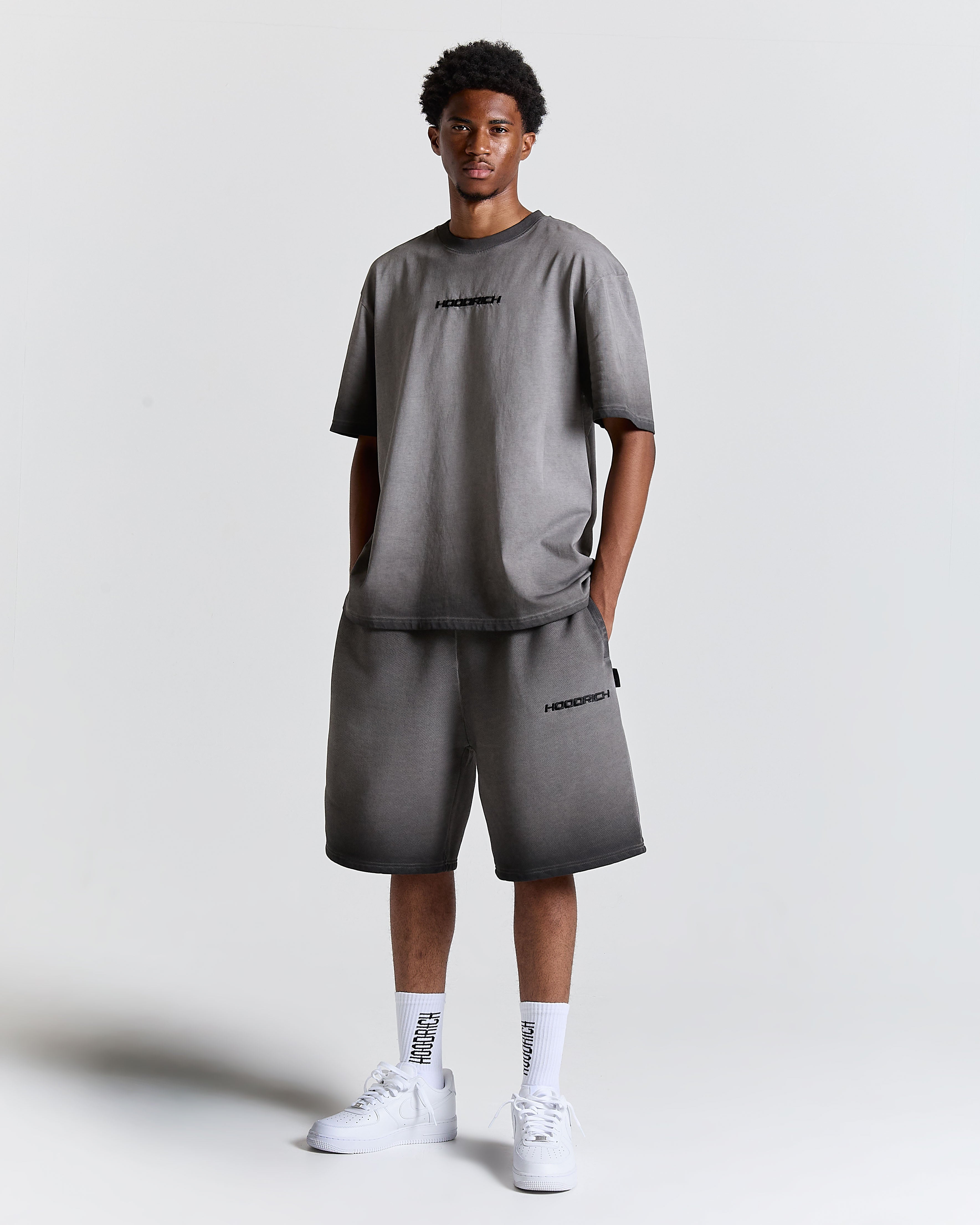 Model wearing an oversized black oil wash t-shirt and matching shorts with Hoodrich logos, white socks, and white trainers.
