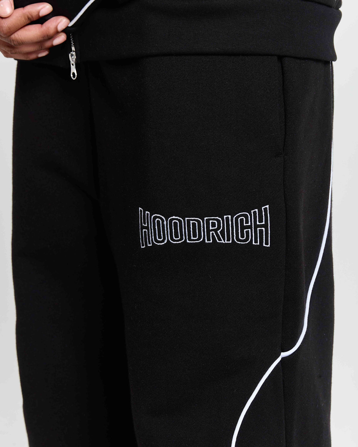 Close-up of the white outlined Hoodrich logo embroidered on a model wearing oversized black joggers.