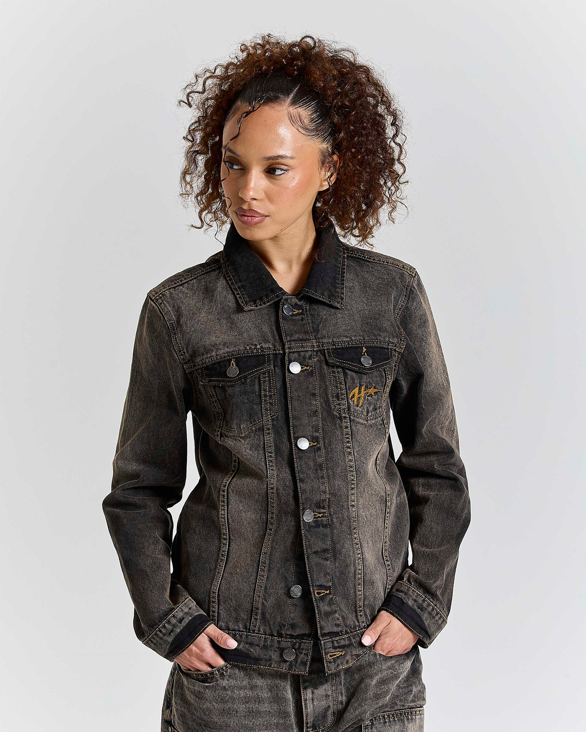 Woman wearing a dark denim jacket with a brand logo on a light gray background