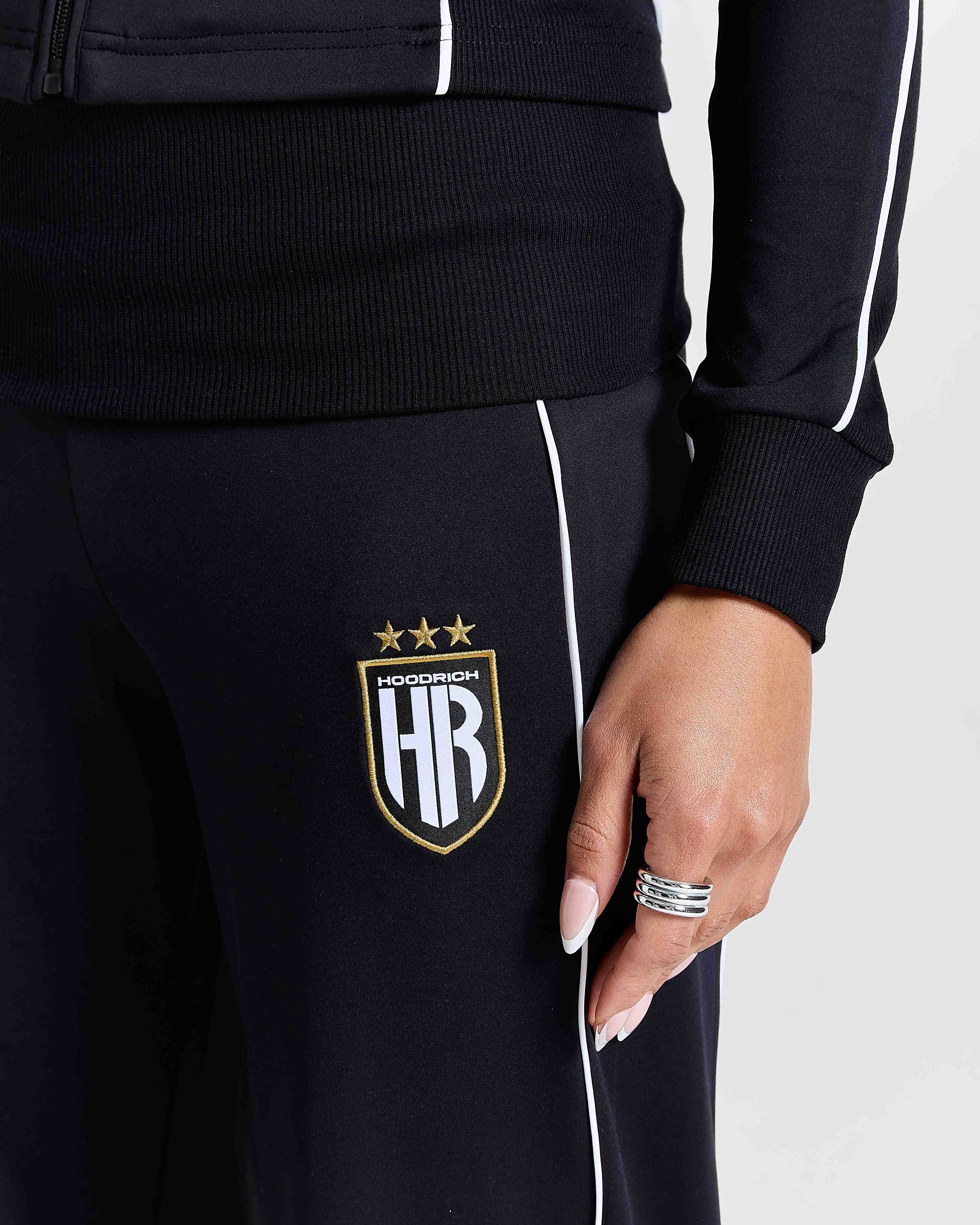 Displays a model wearing the Black 'Hoodrich' branded women's Glide Football Full Tracksuit