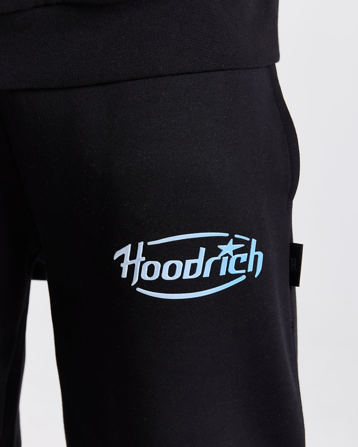 Displays a model wearing the Black 'Hoodrich' branded men's Curve Full Tracksuit featuring the details on the branding