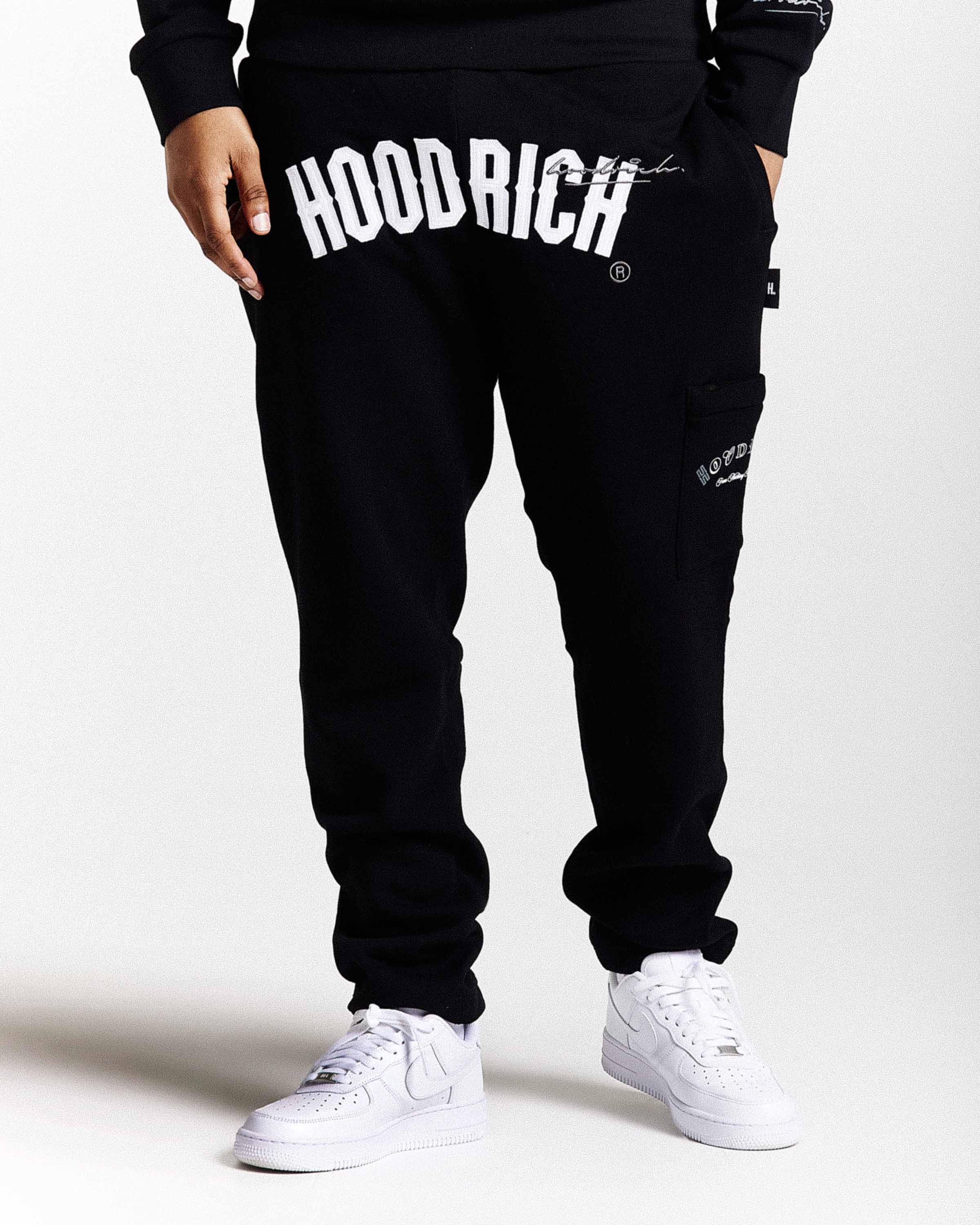 Displays a model wearing the Black 'Hoodrich' branded men's Stature Full Tracksuit