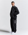 Person wearing a black tracksuit with white piping on a light gray background