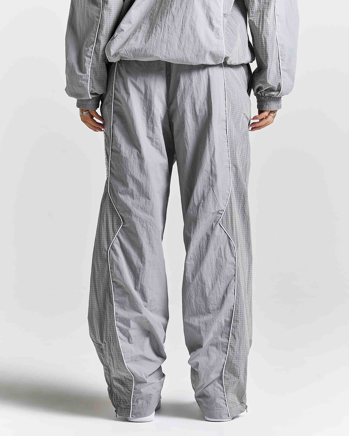 A person shown from the back wearing loose, wide-leg gray textured pants and a matching gray top against a plain light gray studio background.
