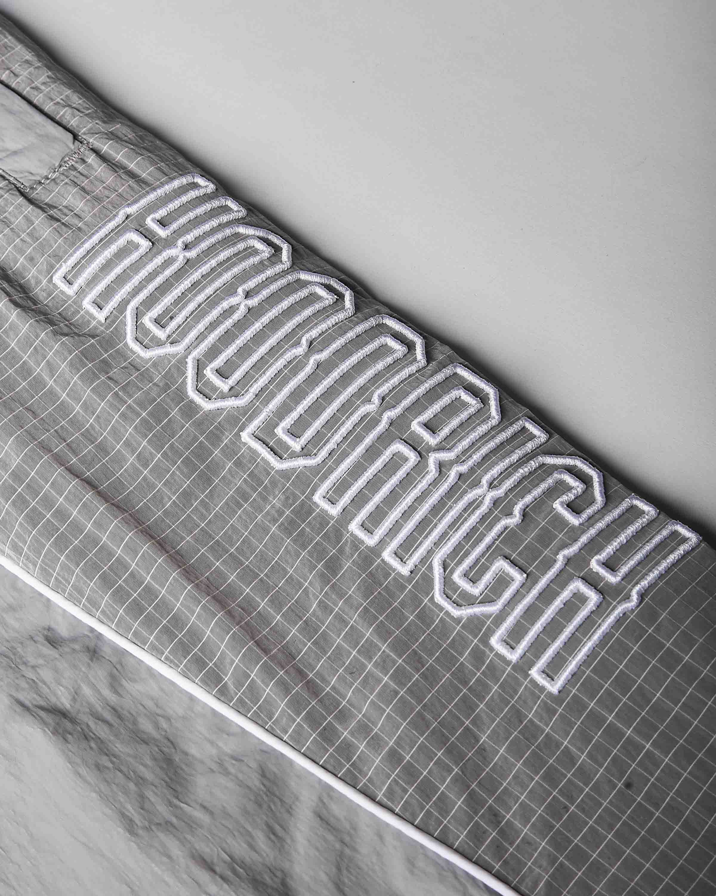 Close-up of a gray grid-patterned fabric item, likely a blanket or comforter, featuring large white varsity-style outlined lettering that reads 'HOODRICH'.
