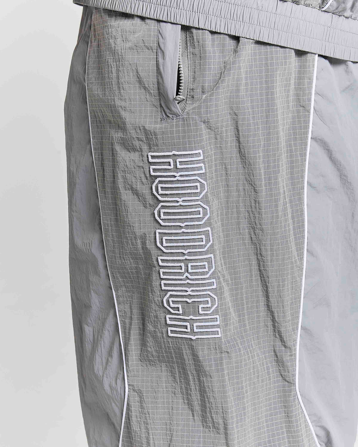 Close-up of gray Hounddog windbreaker shorts with a white outlined vertical logo on the leg, featuring a zippered pocket and white piping.
