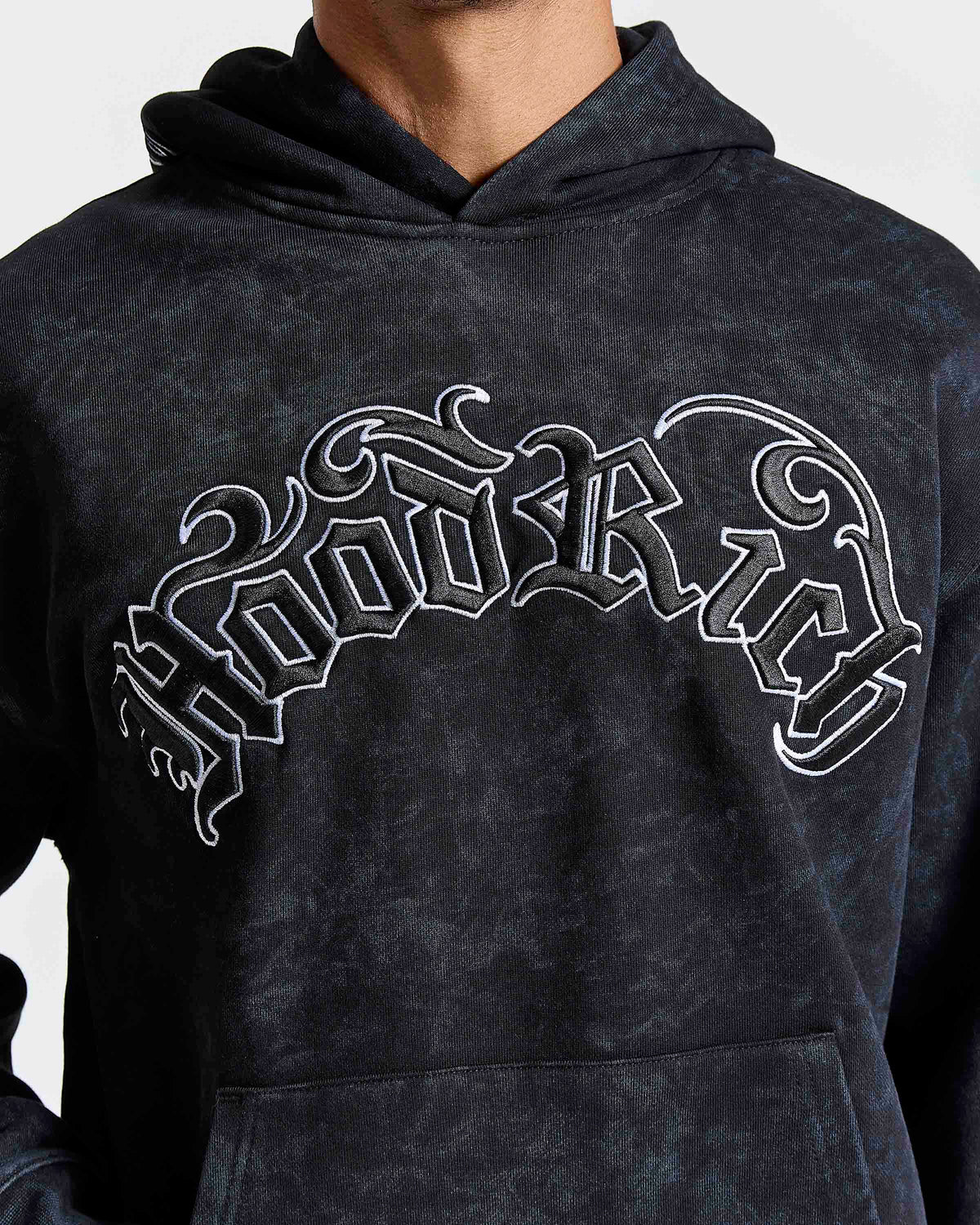 A close-up of a person wearing a dark washed hoodie with a large white gothic-style 'Hoodrich' graphic across the chest.