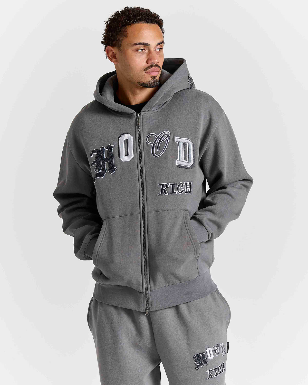 Displays a model wearing the Grey 'Hoodrich' branded men's Forza Full Tracksuit 
