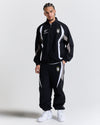 Male model wearing a black tracksuit with white accents on a light gray background