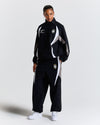 Person wearing a black tracksuit with white and gray accents on a light gray background