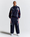 Person wearing a navy tracksuit with red and white accents on a light gray background