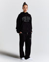 Person wearing a black tracksuit with 'Hood Rich' branding on a light gray background