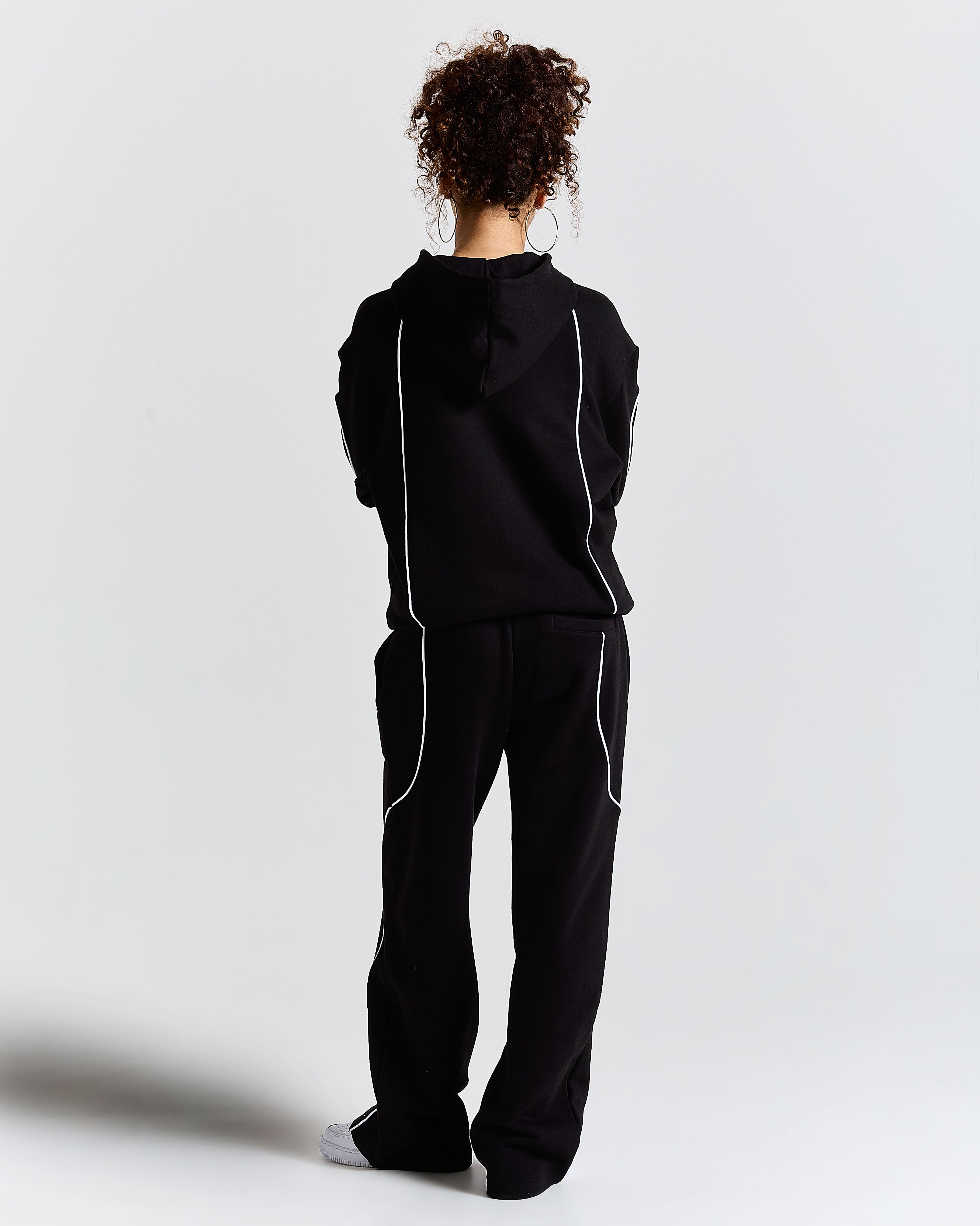 Person wearing a black tracksuit with white stripes on a light gray background