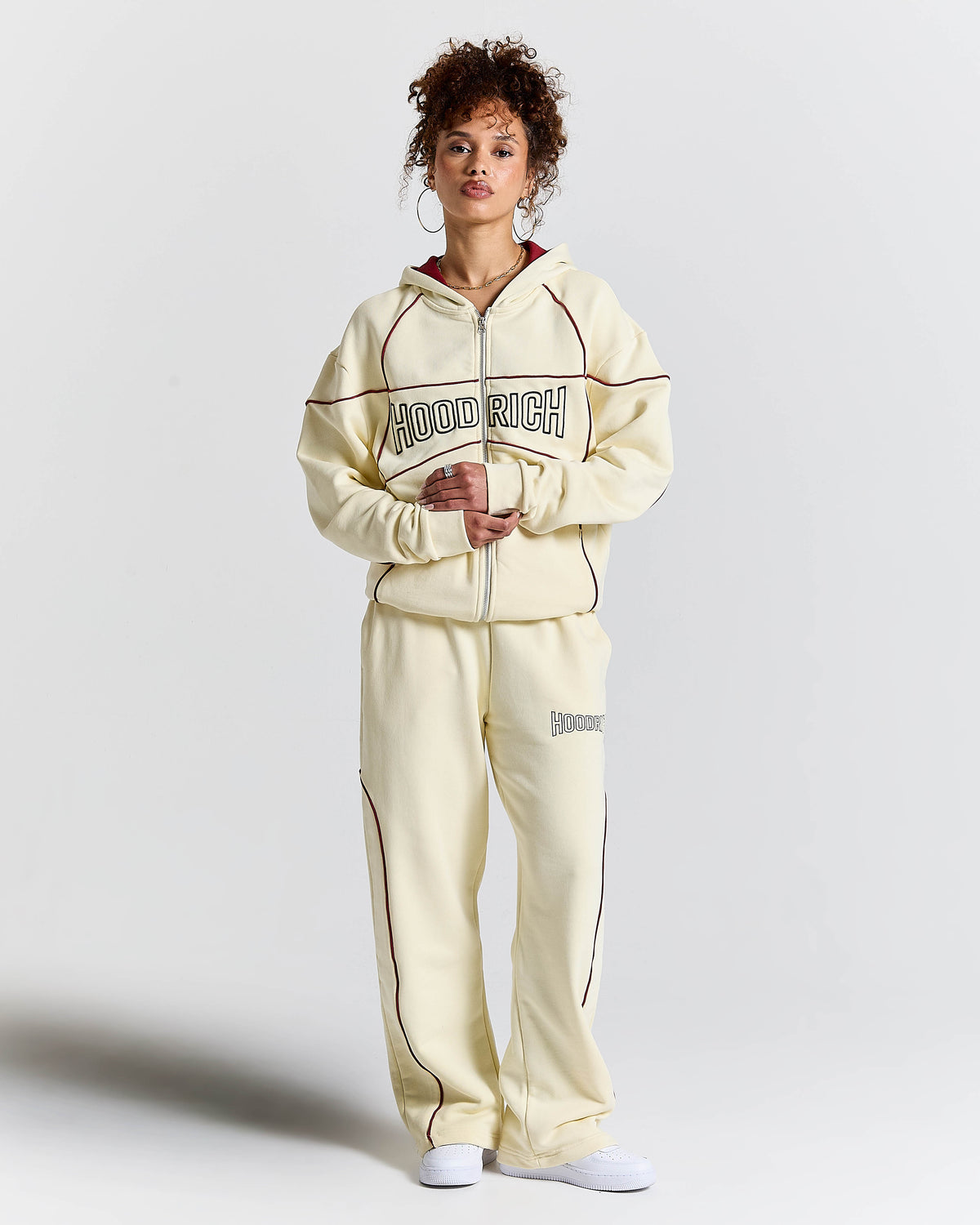 Person wearing a cream tracksuit with 'Hoodrich' branding on a light gray background