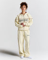 Person wearing a cream tracksuit with 'Hoodrich' branding on a light gray background