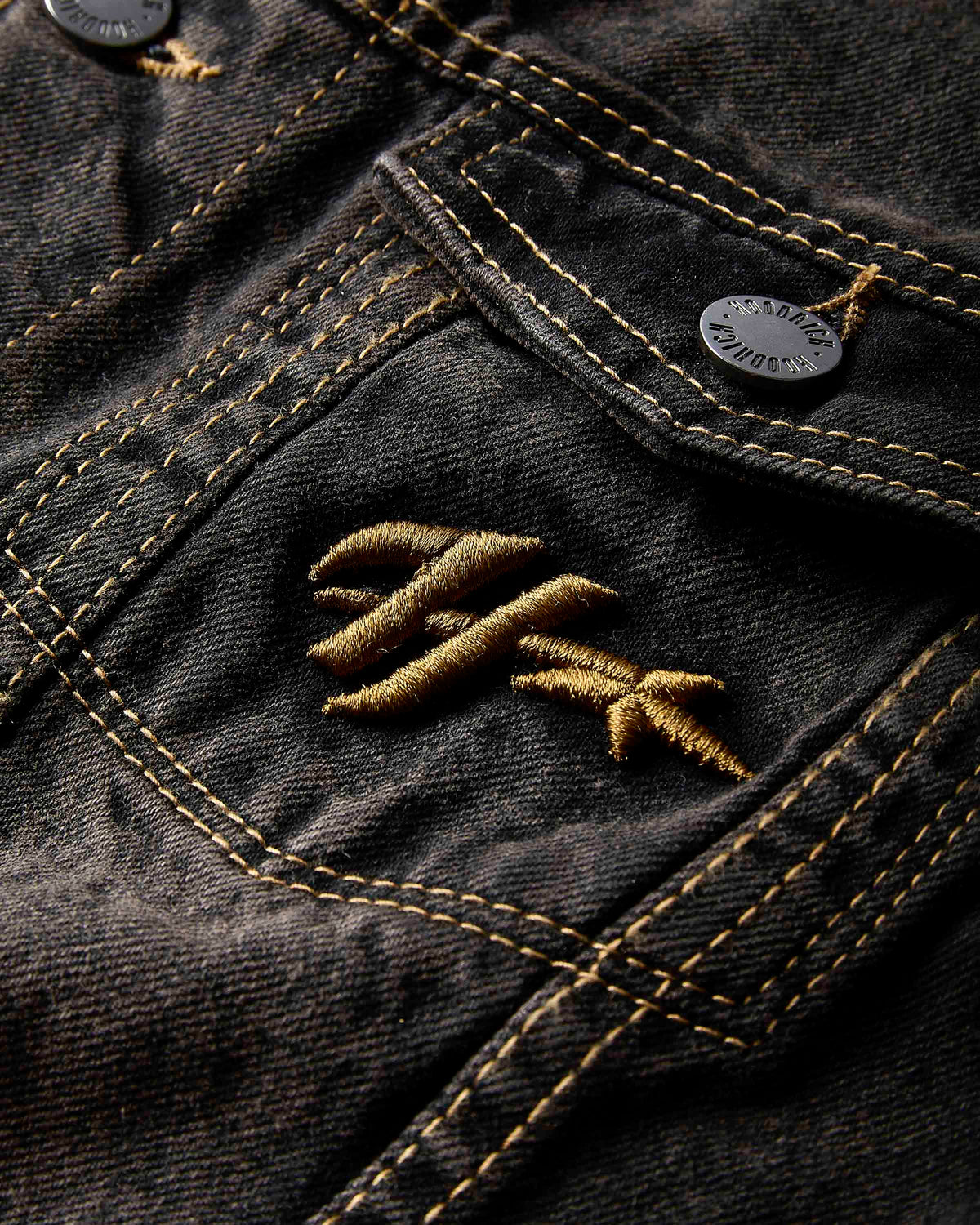Close-up of a dark denim jacket with an embroidered logo on the pocket.