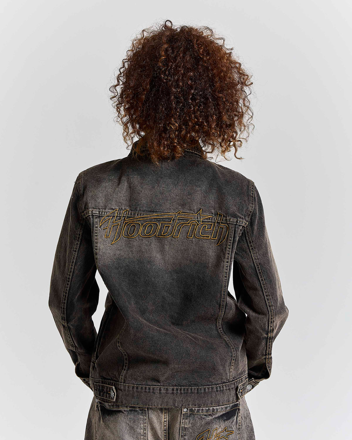 Person wearing a black denim jacket with 'Hoodrich' branding on the back against a white background