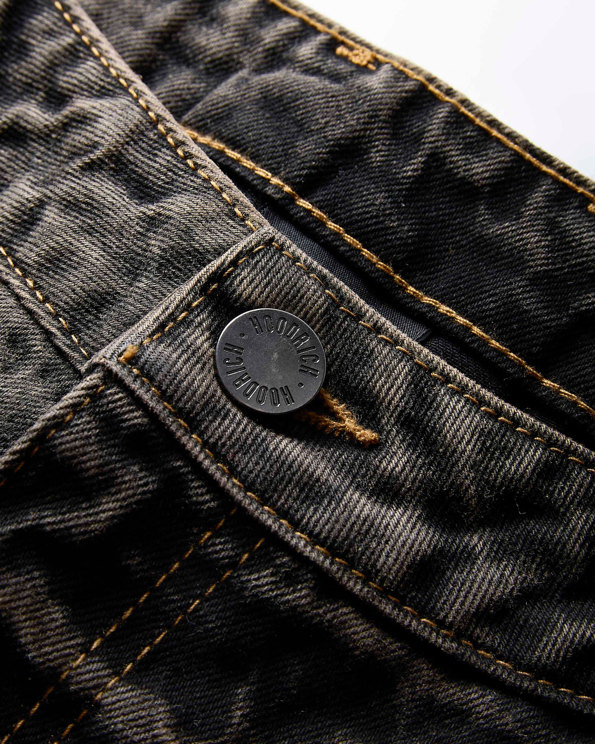 Close-up of dark gray washed denim jeans showing the button closure, contrast gold stitching, and detailed denim texture.