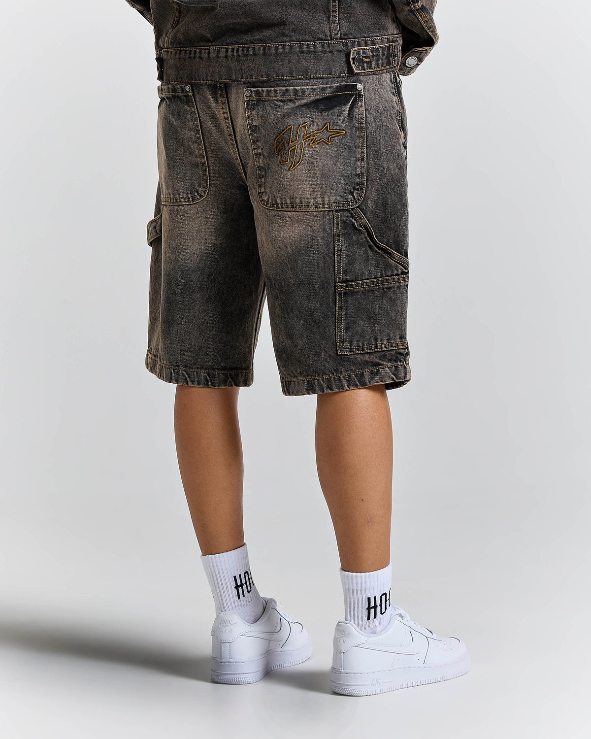 Person wearing dark denim shorts and white sneakers with 'HOODRICH' socks on a light gray background