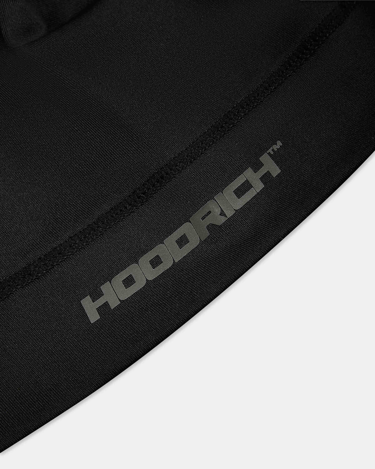 Close-up of a black fabric product with a gray HOODRICH logo printed diagonally across it, set against a light gray background.