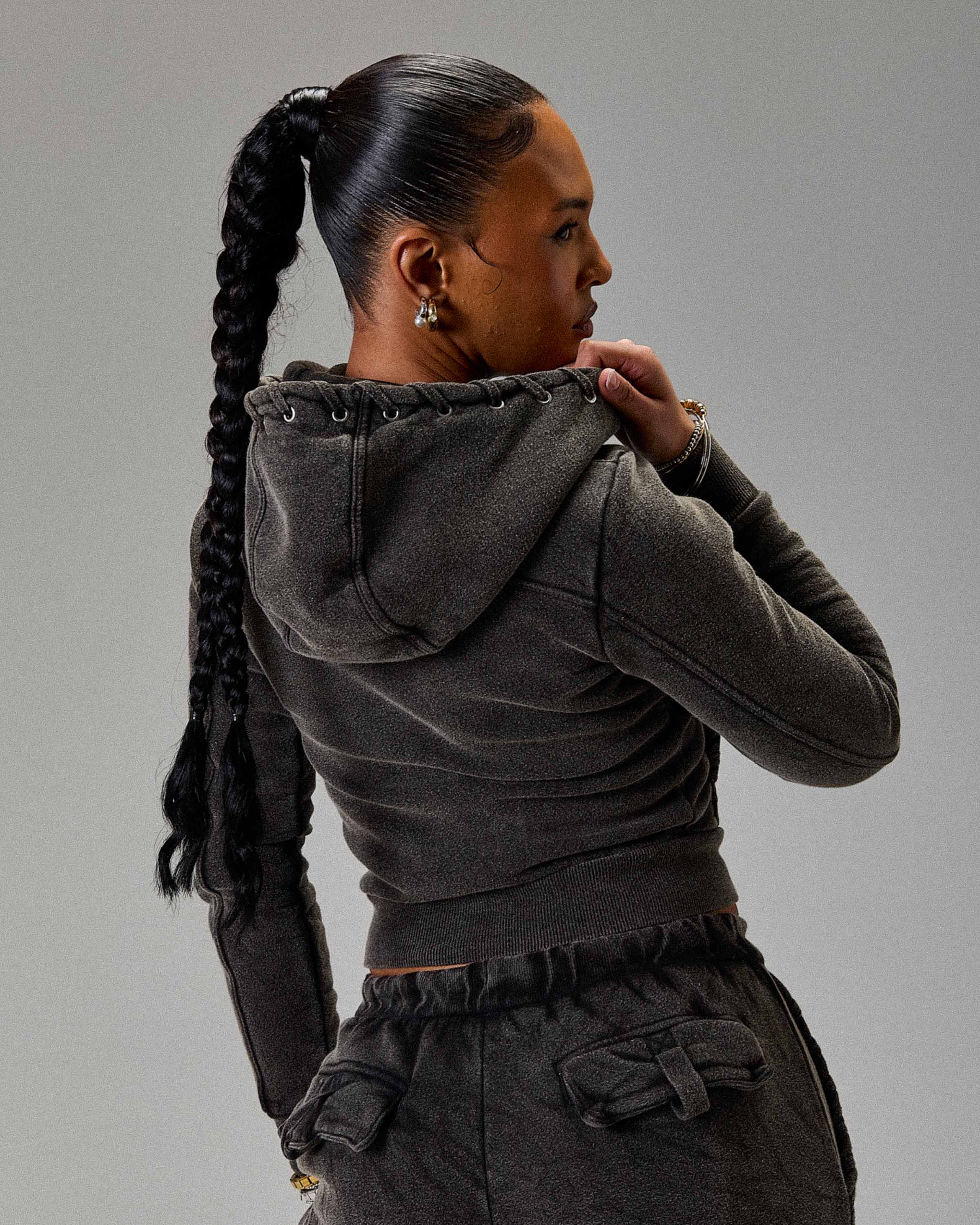 Woman wearing a dark gray hoodie and pants against a plain background