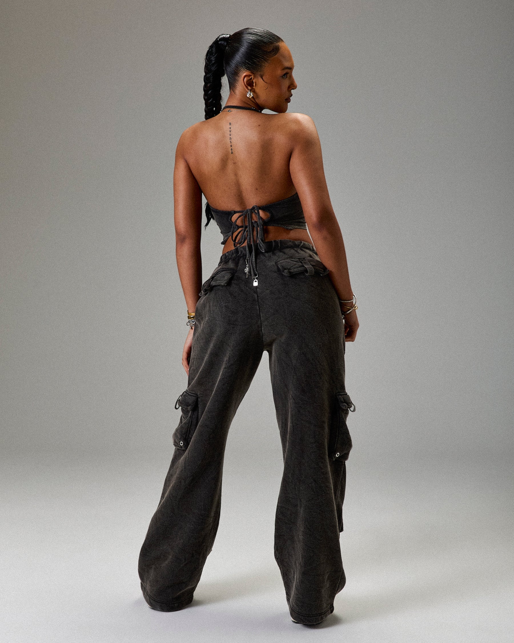 Person wearing a black outfit with wide-leg pants and a halter top on a gray background