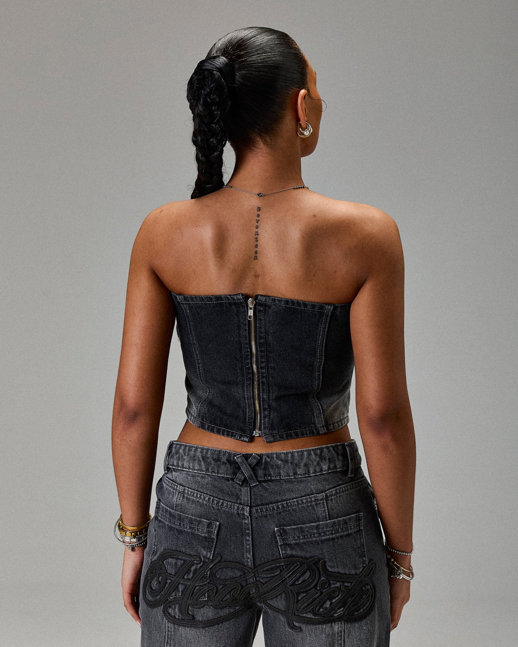 Person wearing a denim strapless top and high-waisted jeans on a gray background