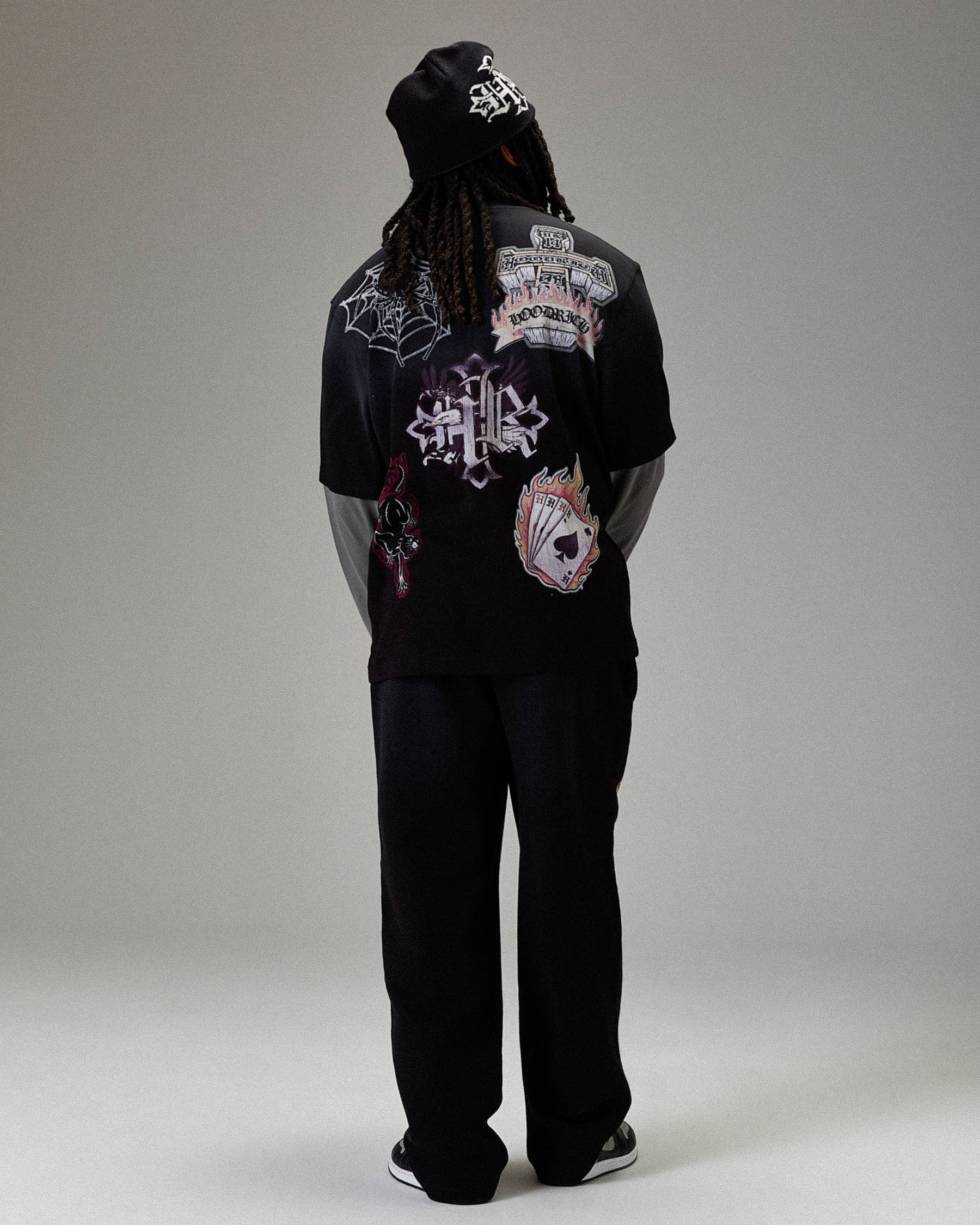 Person wearing a black hoodie with intricate designs on the back against a gray background