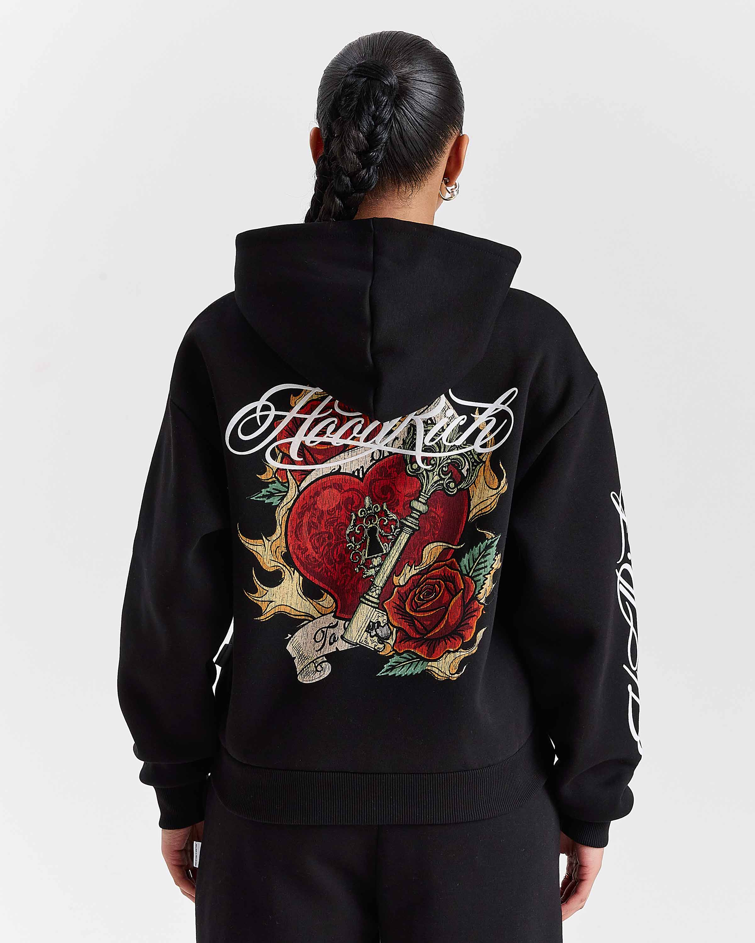 Person wearing a black hoodie with intricate designs and text on the back against a white background