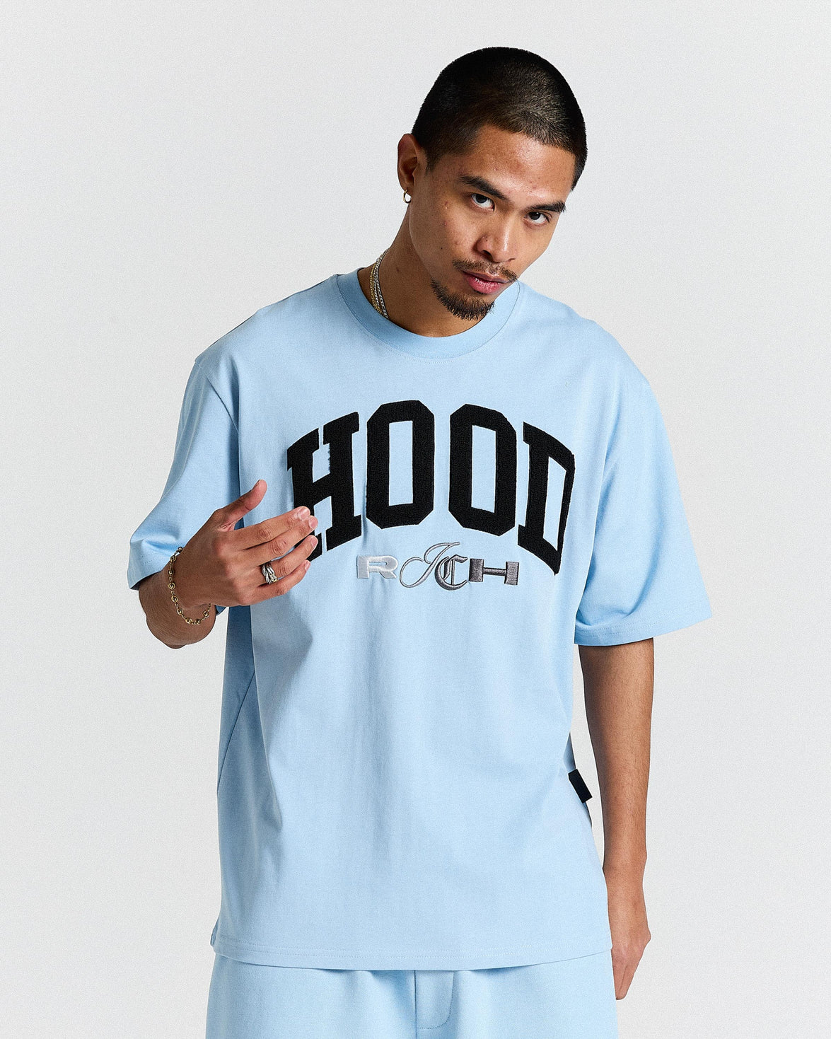 Person wearing a light blue t-shirt with 'HOODRICH' text on a plain background