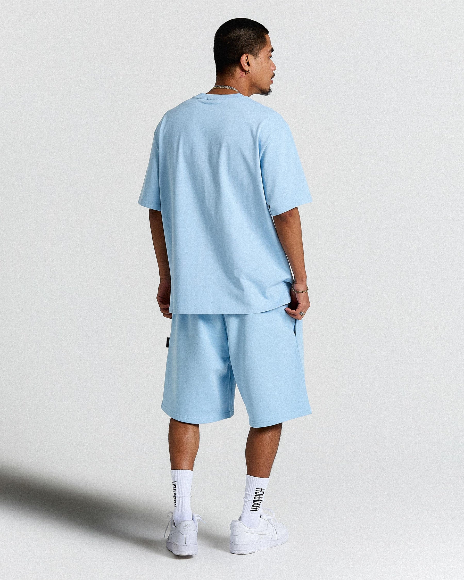 Person wearing a light blue outfit with shorts and a t-shirt on a plain background