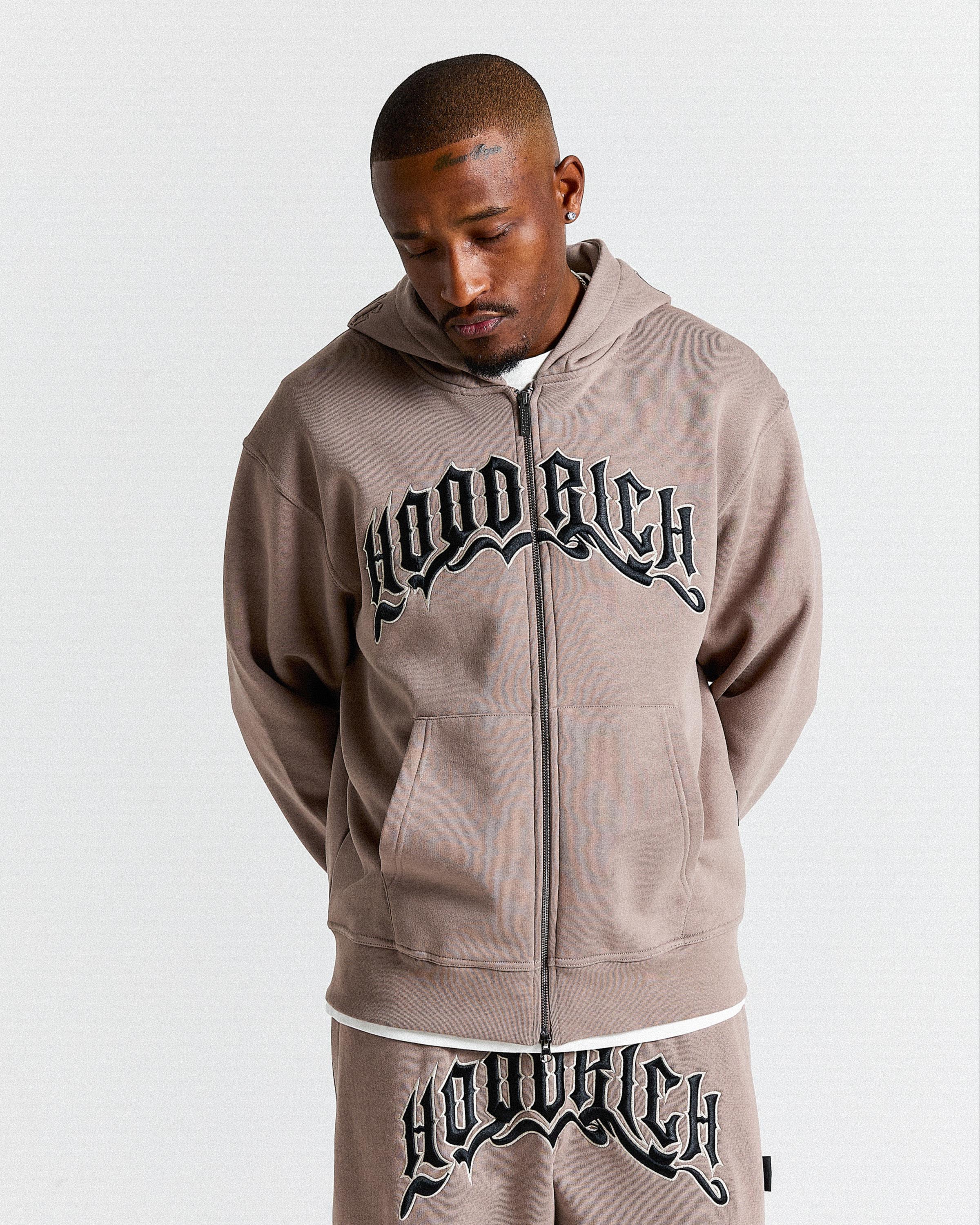 Man wearing a 'Hood Rich' hoodie and pants on a light gray background