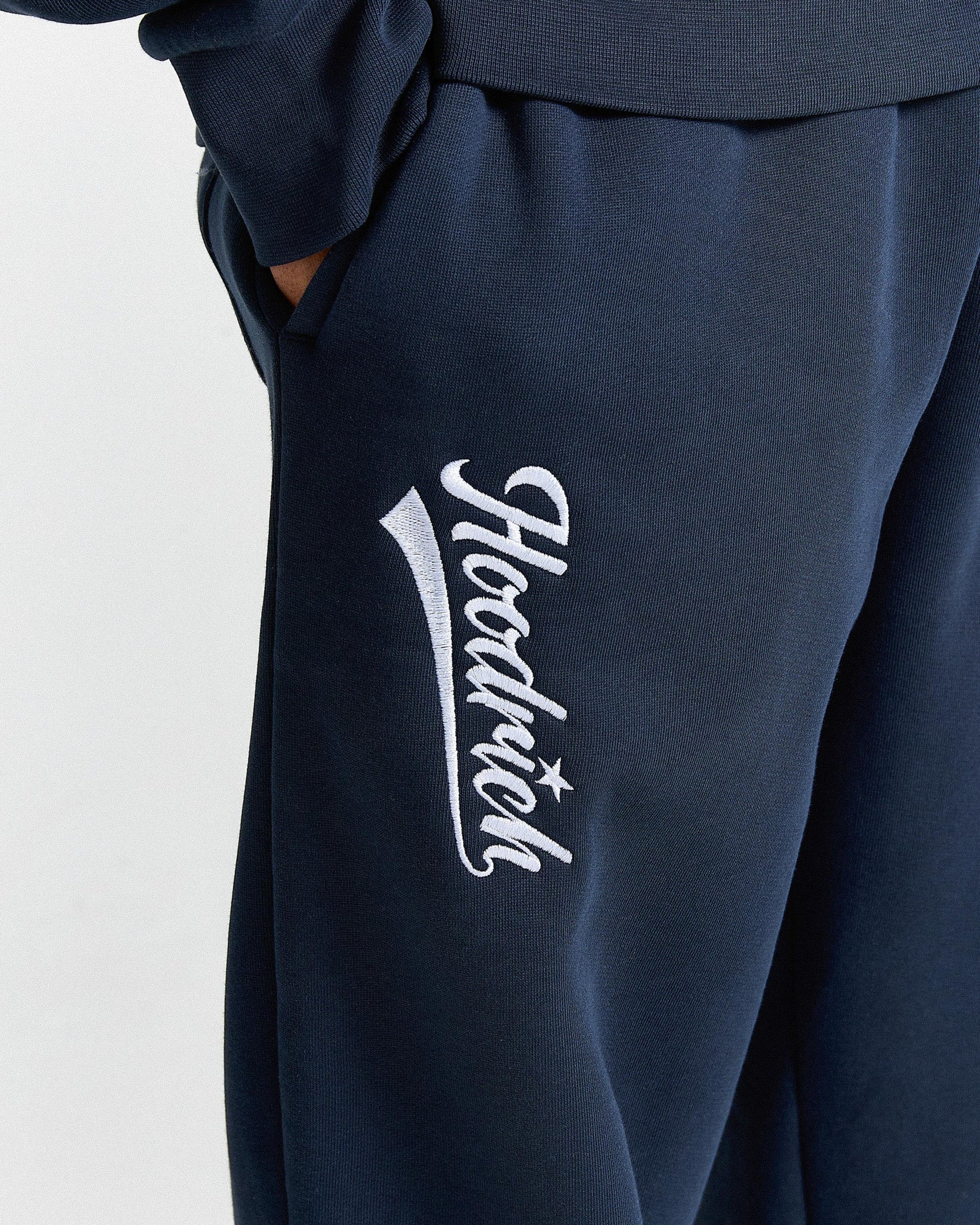 Navy blue sweatpants with a white logo on a light gray background