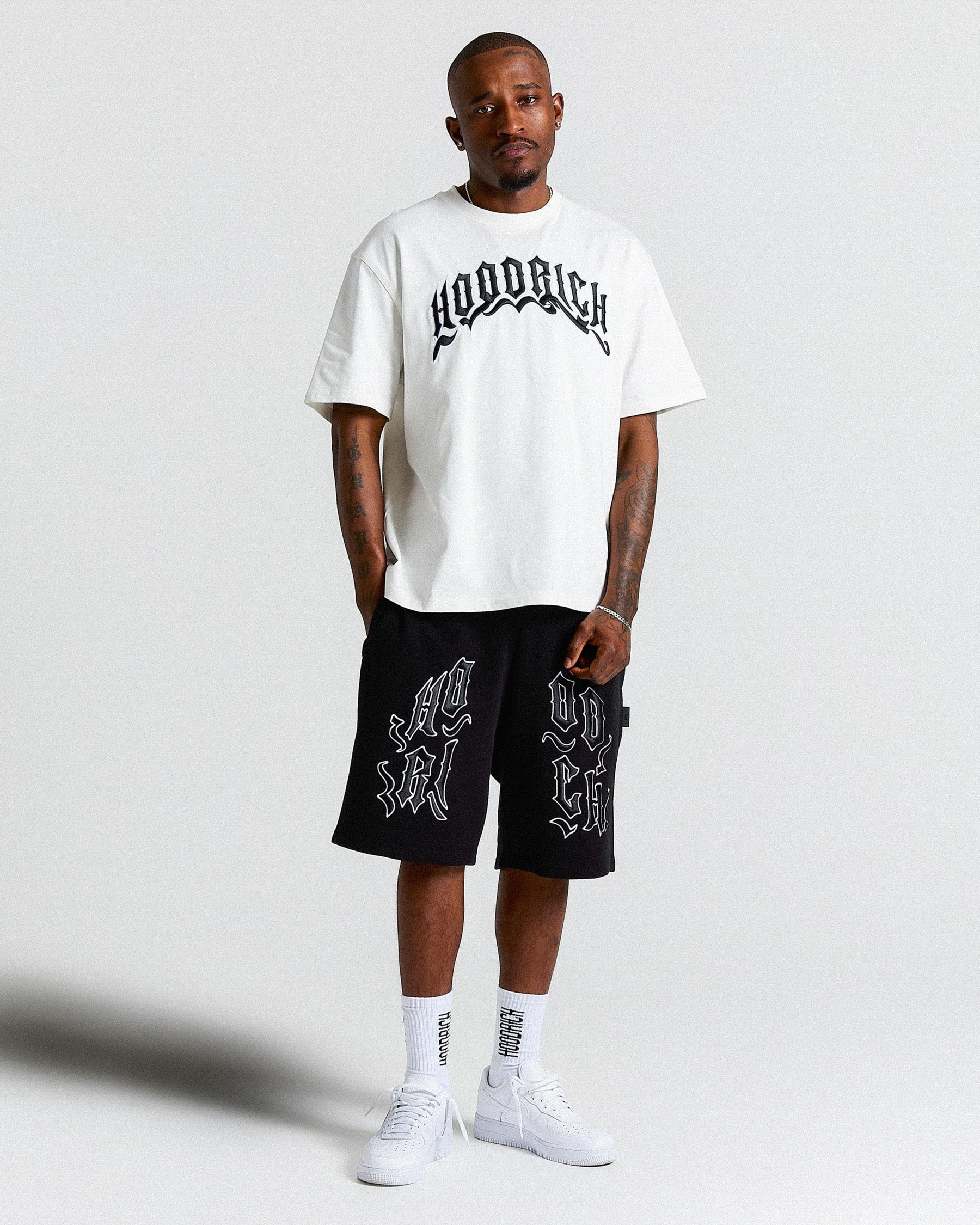 Person wearing a white t-shirt and black shorts with branding on a light gray background