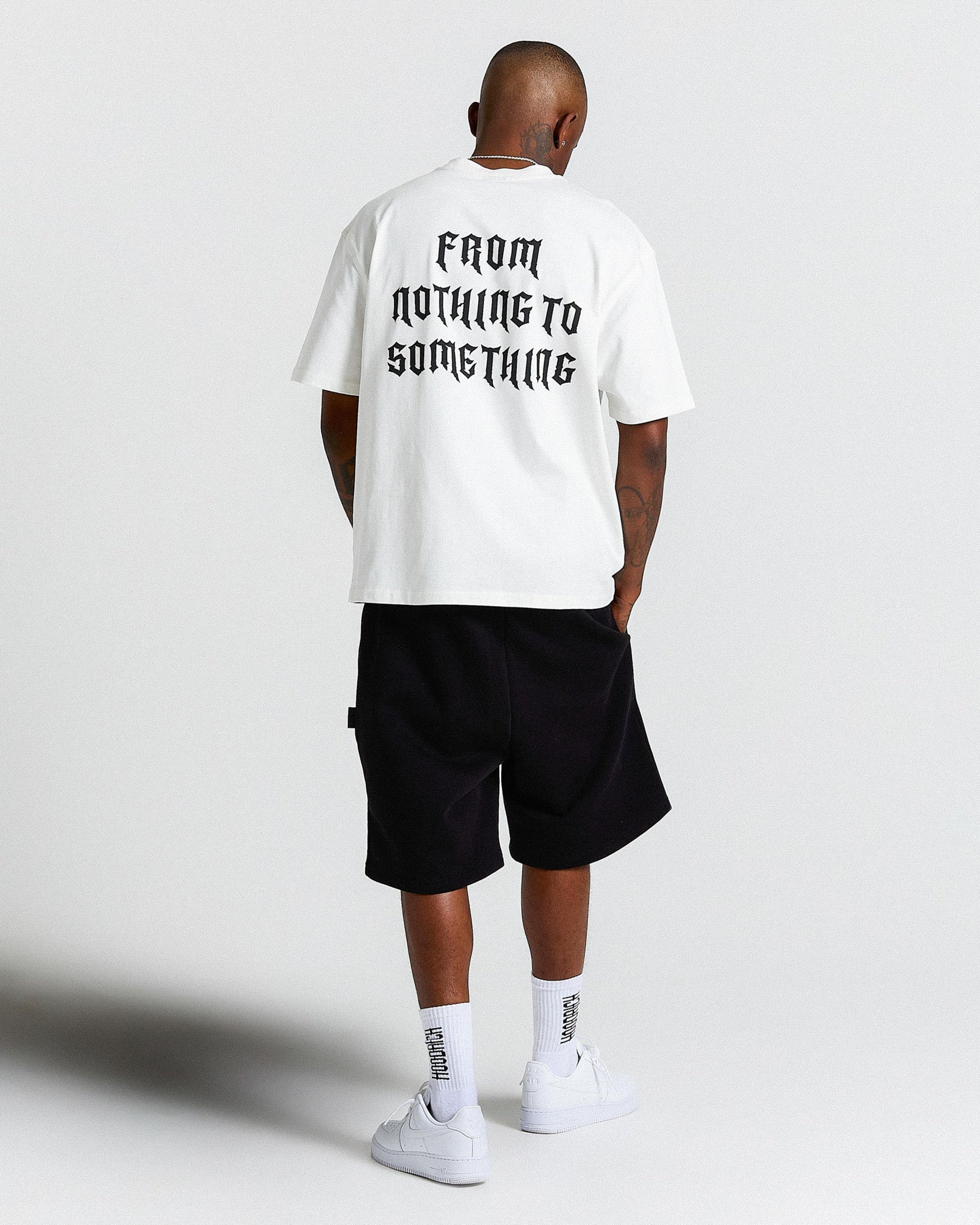 Man wearing black shorts and a white 'HOODRICH' branded short sleeve T-Shirt, with text reading 'From Nothing To Something' across the back.
