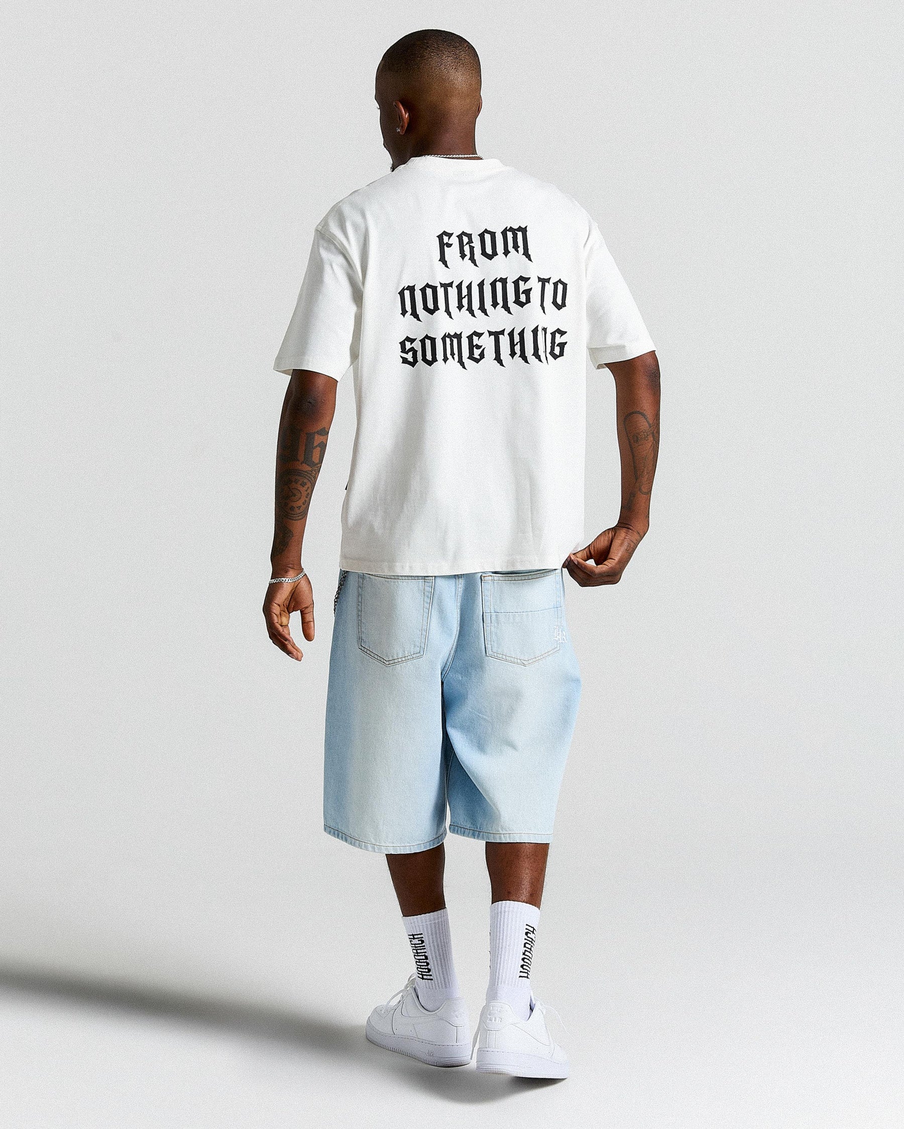 Person wearing a white t-shirt with text and light blue shorts on a plain background