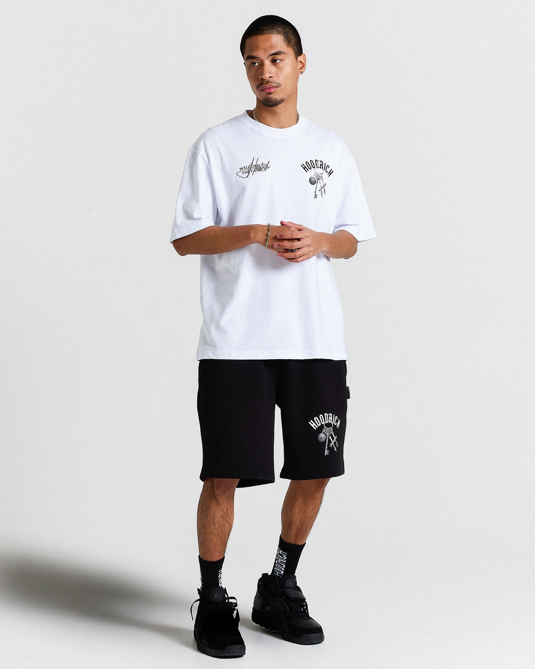 Person wearing a white t-shirt and black shorts with branding on a plain background