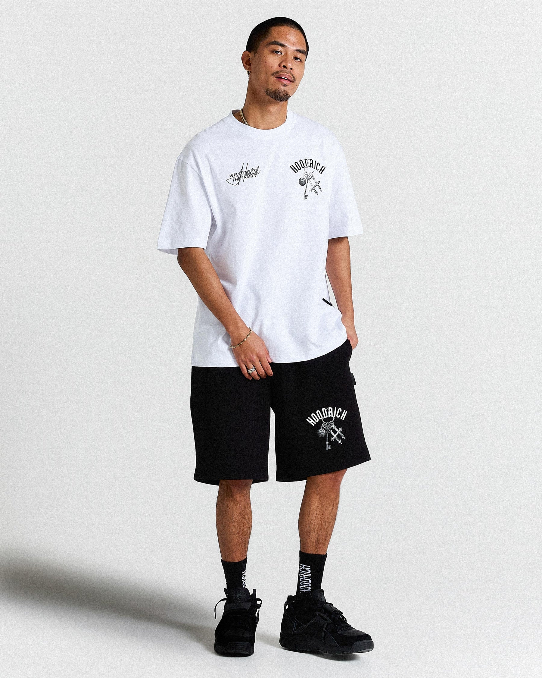 Man wearing a white t-shirt and black shorts with branding on a plain background