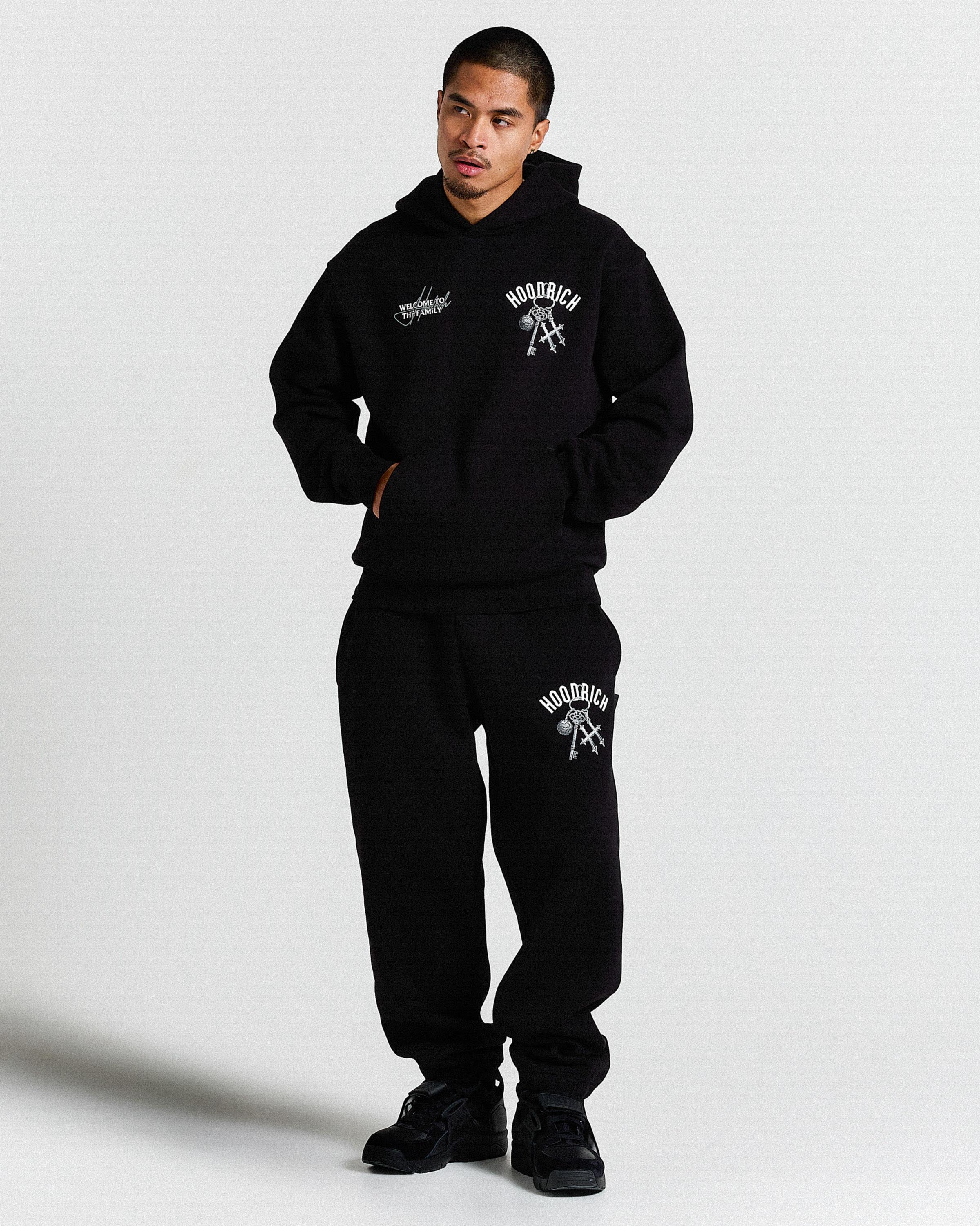 Person wearing a black hoodie and sweatpants set with visible branding on a light gray background