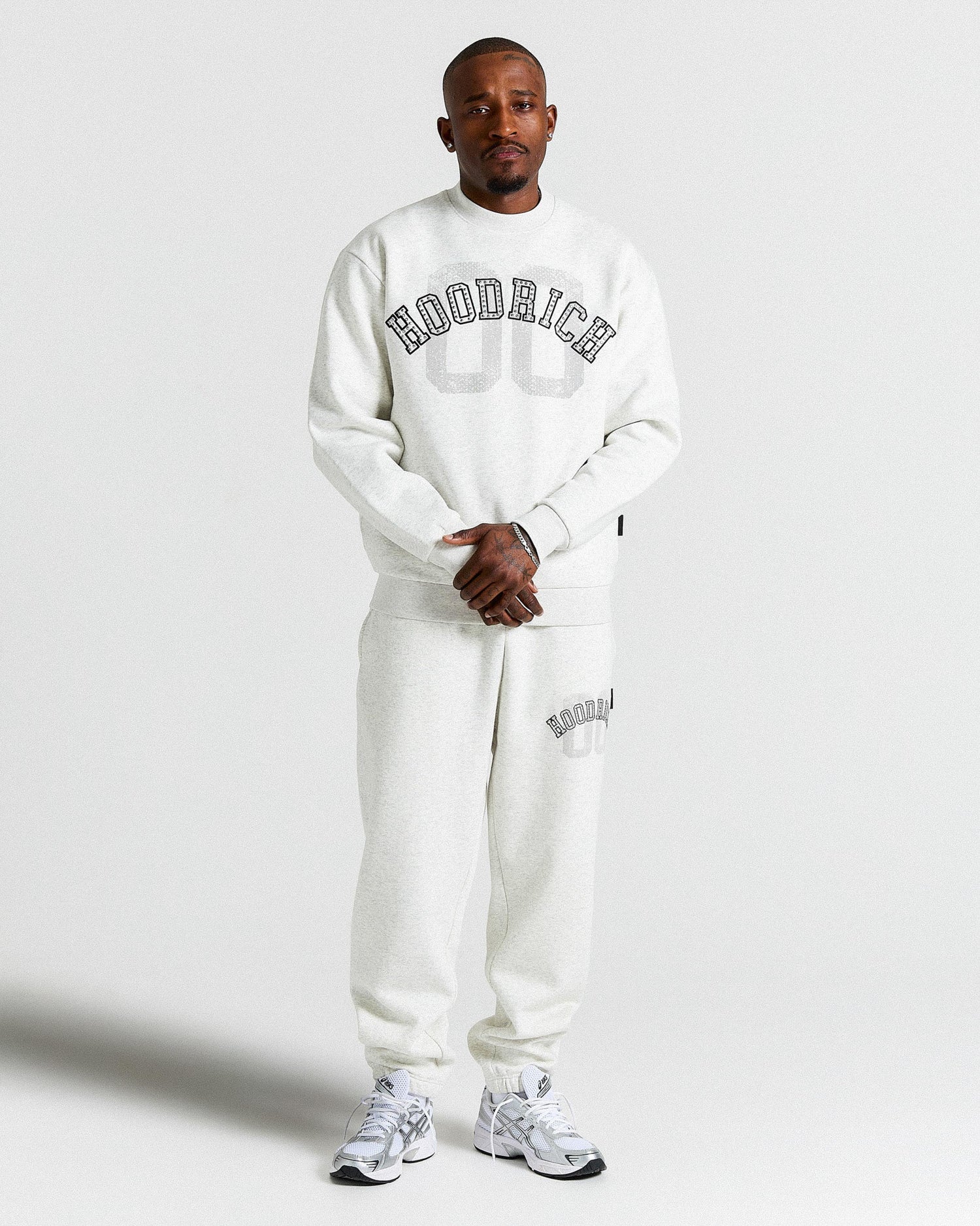 Person wearing a white 'Hoodrich' sweatshirt and pants on a light gray background