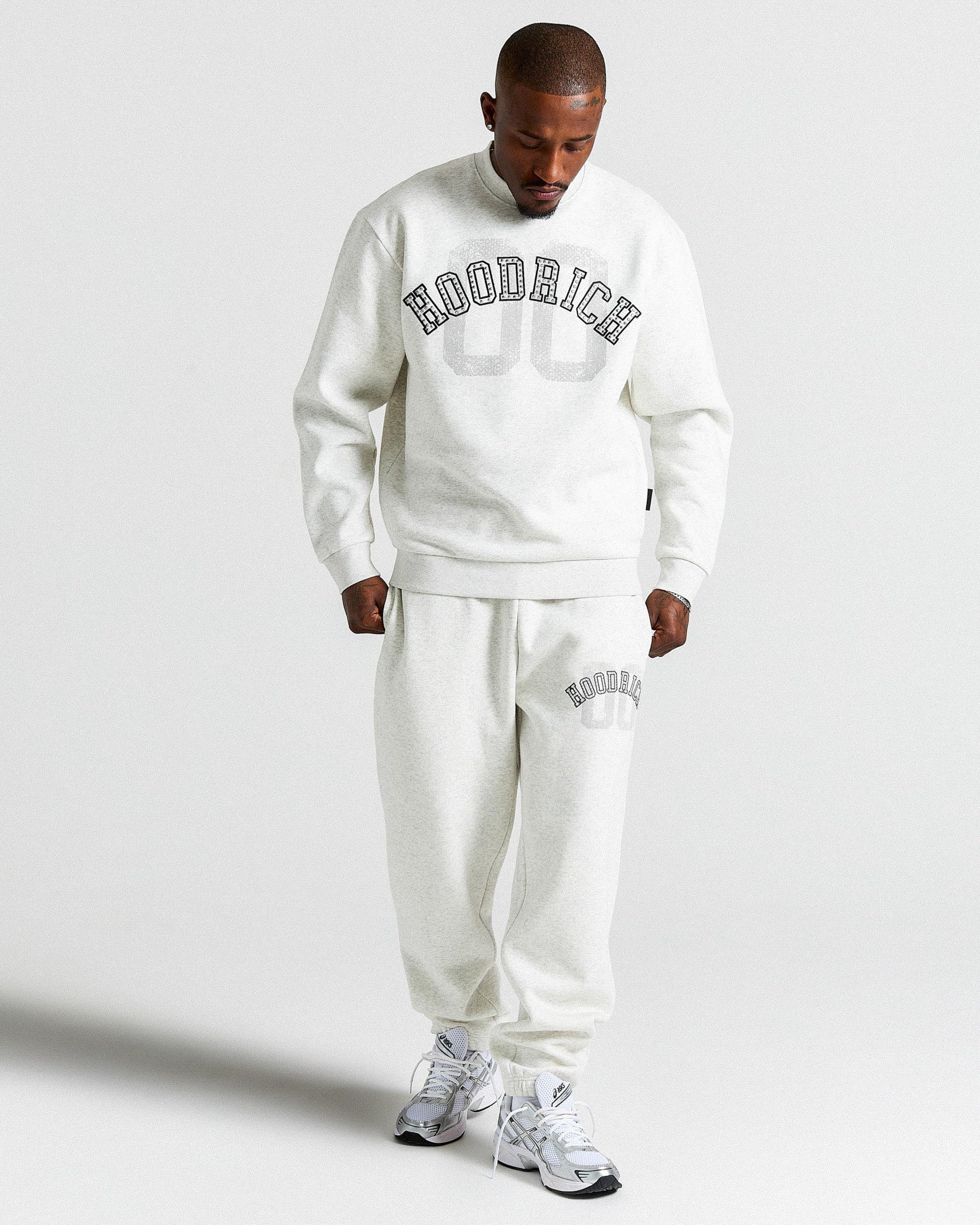 Man wearing a light grey 'HOODRICH' tracksuit on a plain background