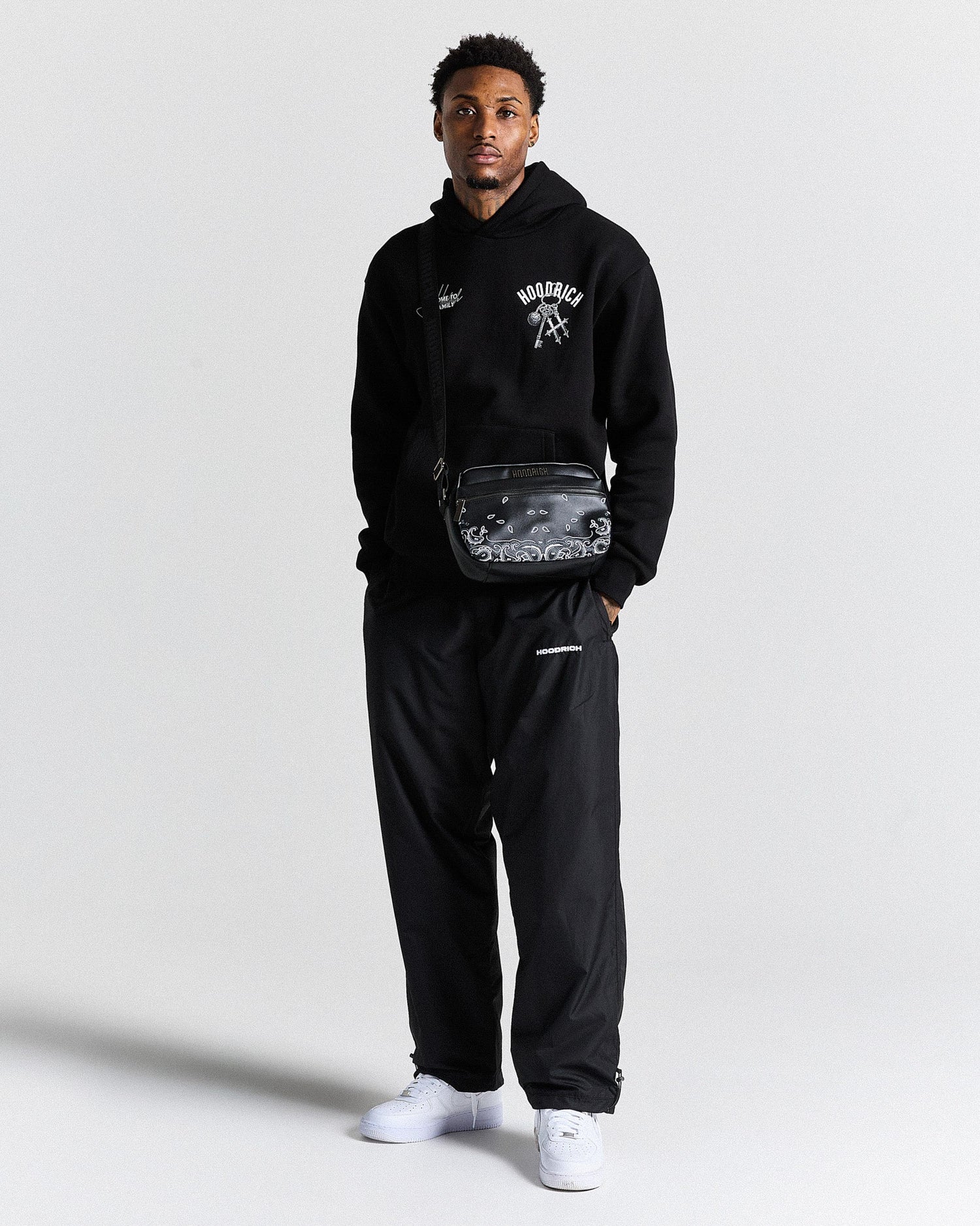 Person wearing a black hoodie and pants with a clear bag, standing against a white background