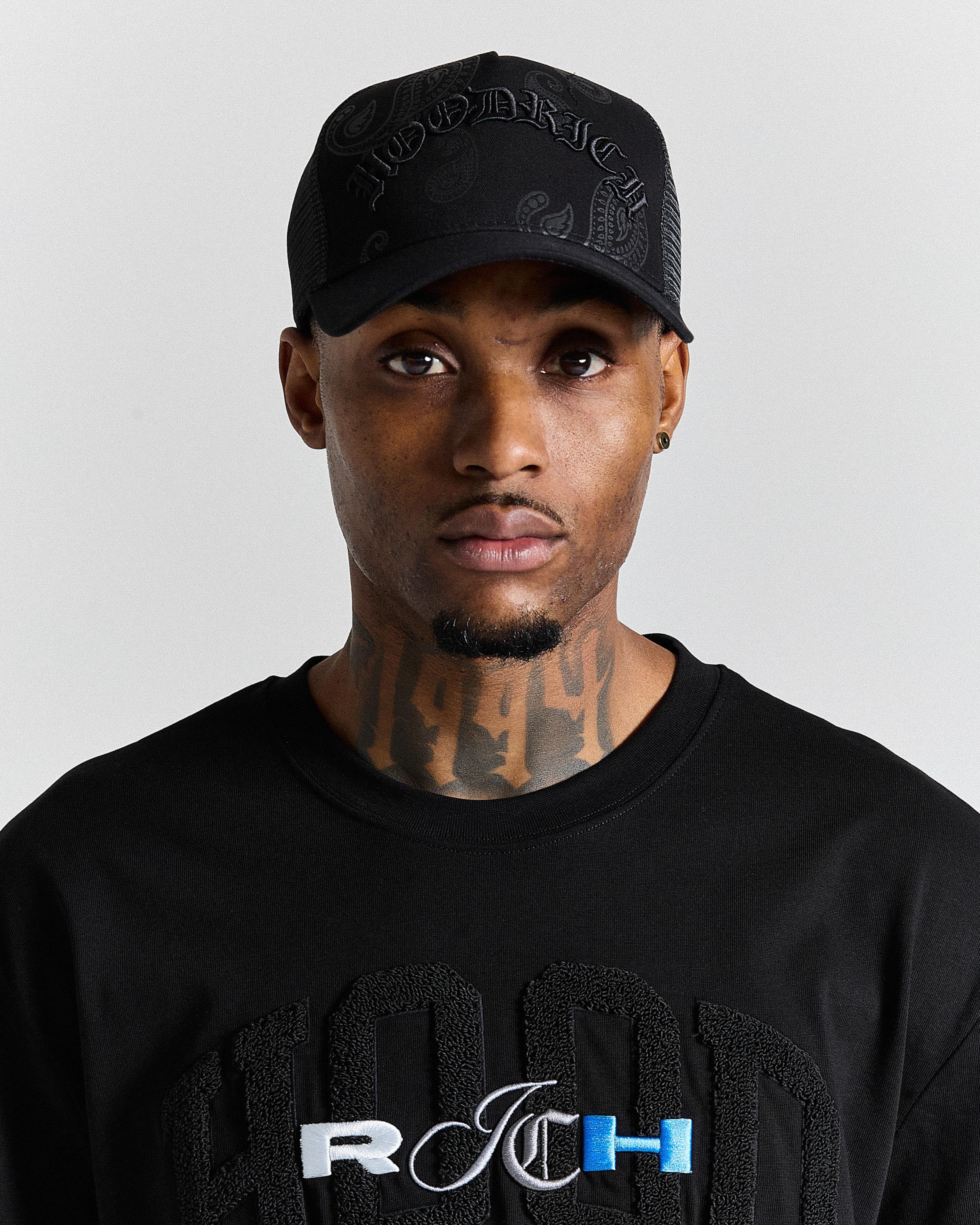 Man wearing a black cap and black shirt with visible branding on a gray background