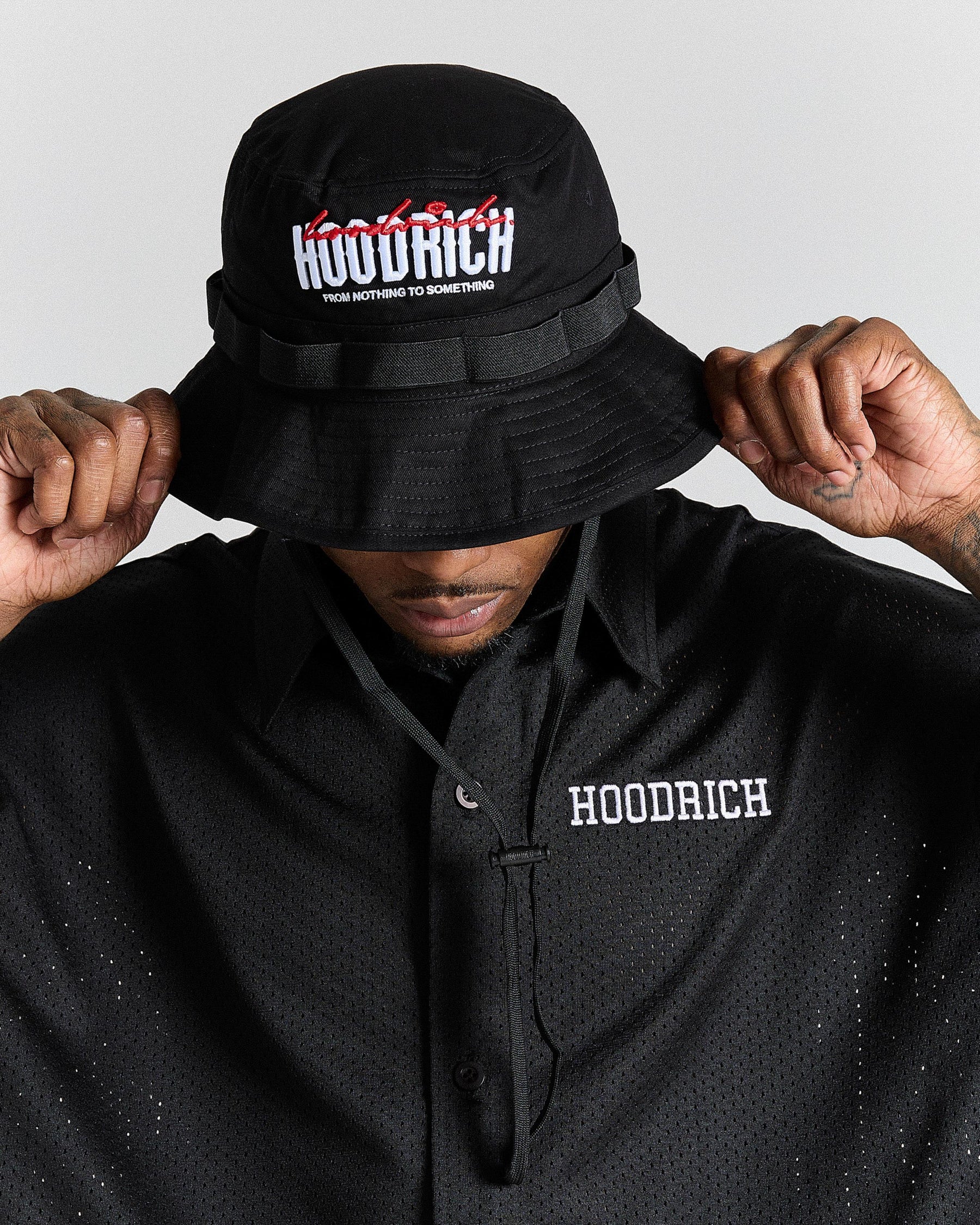 Person wearing a black bucket hat and black polo shirt with 'Hoodrich' branding.