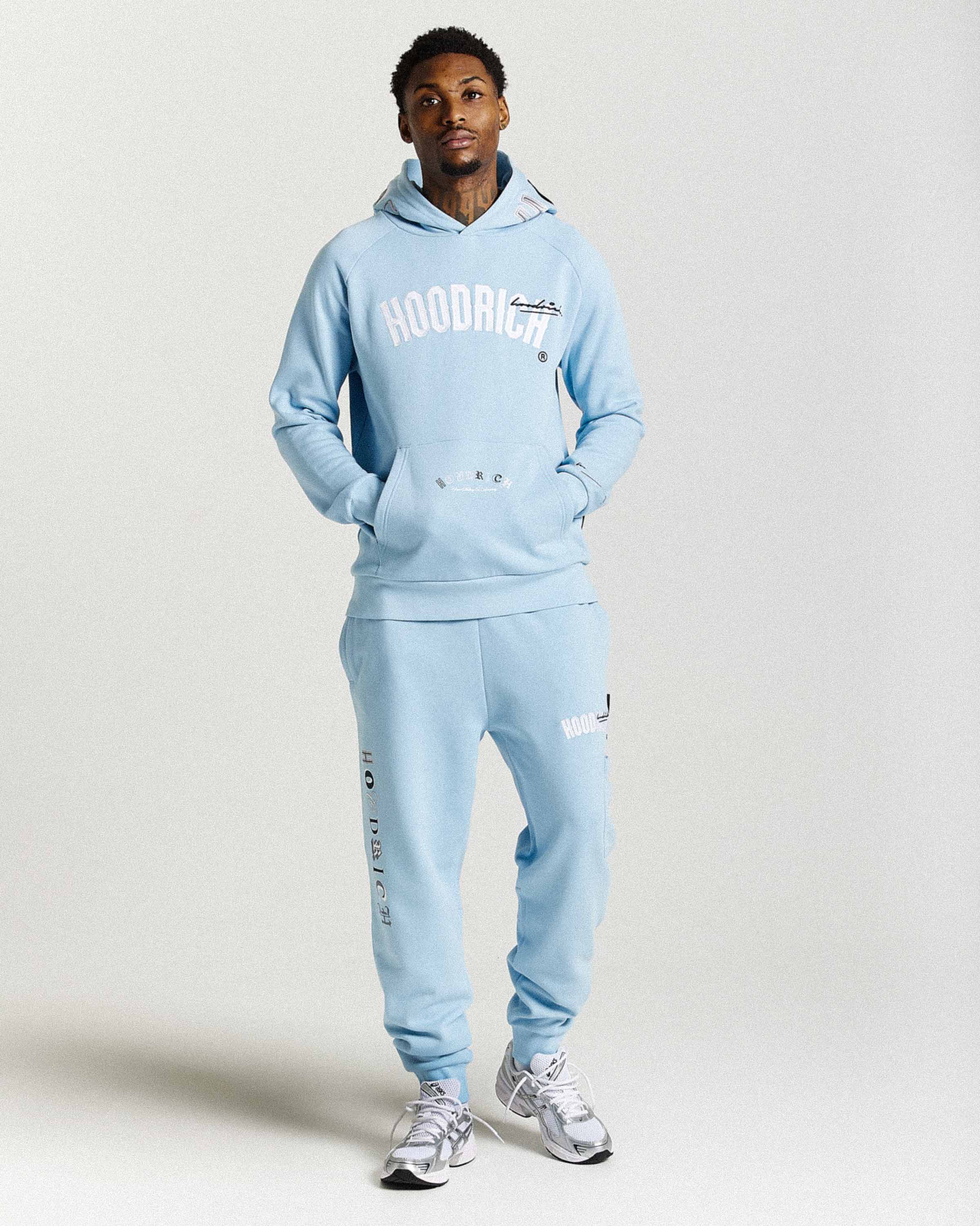 Person wearing a light blue tracksuit with 'HOODRICH' text on a plain background